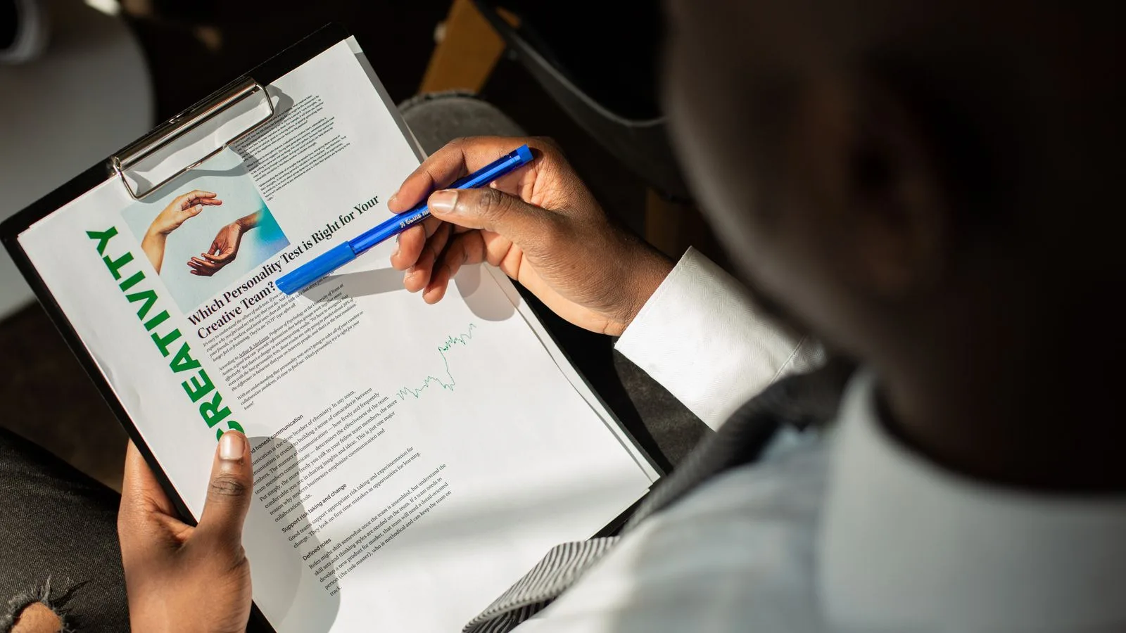 Personne en costume examinant un document sur un clipboard avec un stylo bleu.