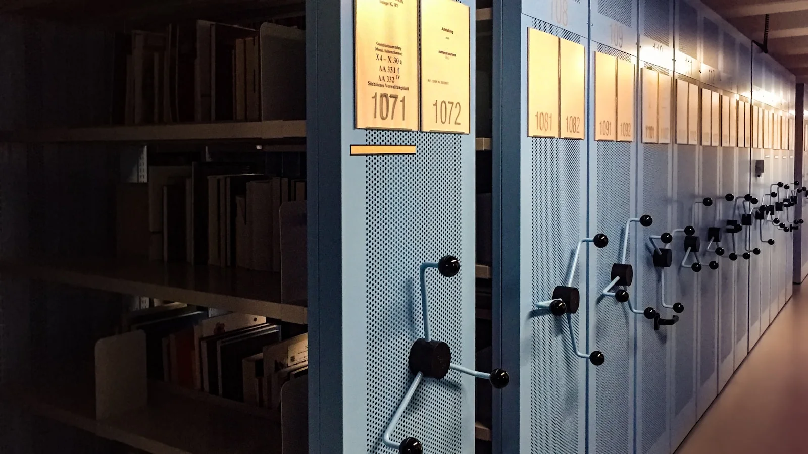 Étagères d'archives remplies de classeurs et de boîtes grises dans une salle de conservation calme.