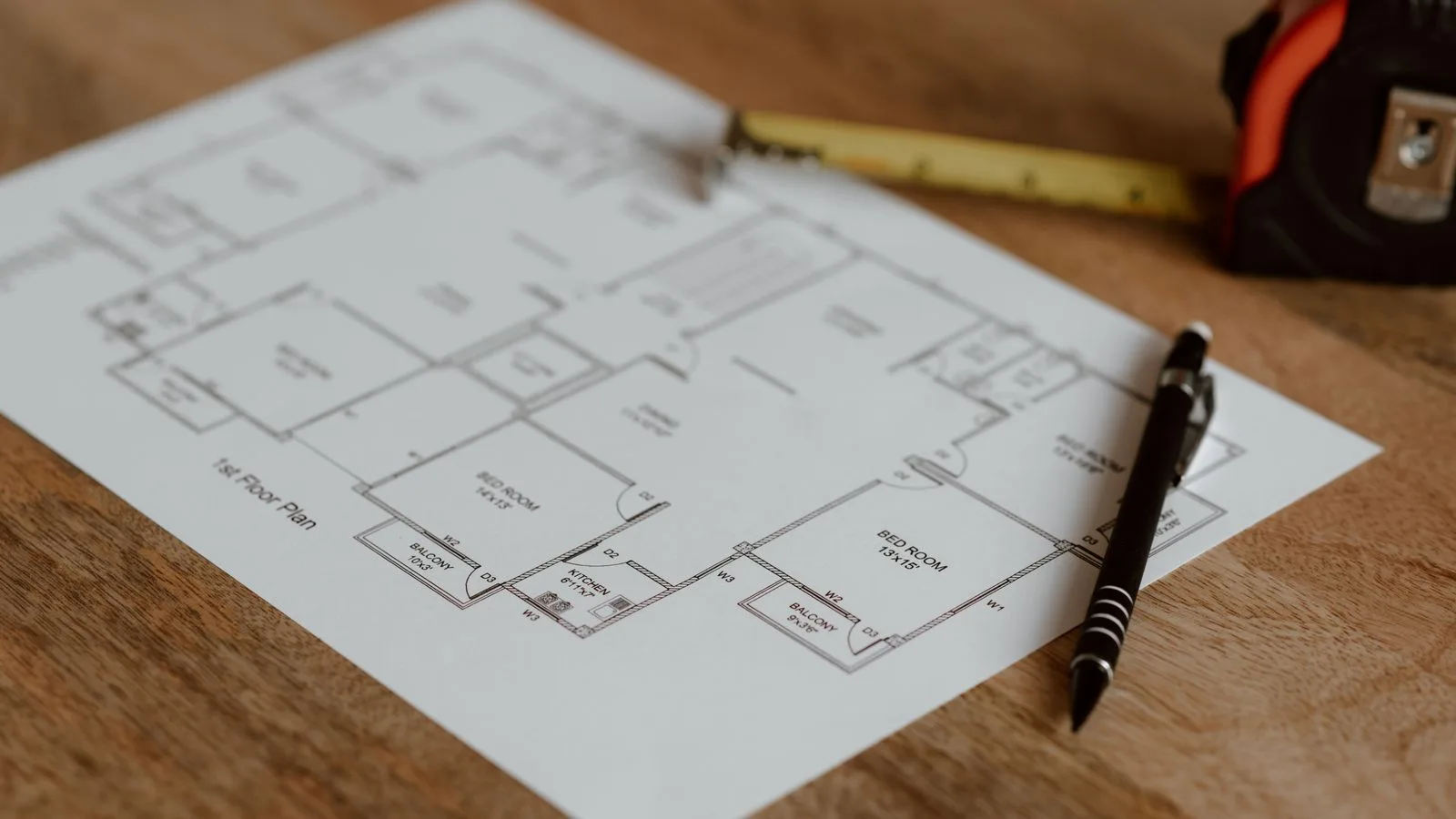 Plan architectural posé sur une table en bois avec un mètre ruban et un stylo.