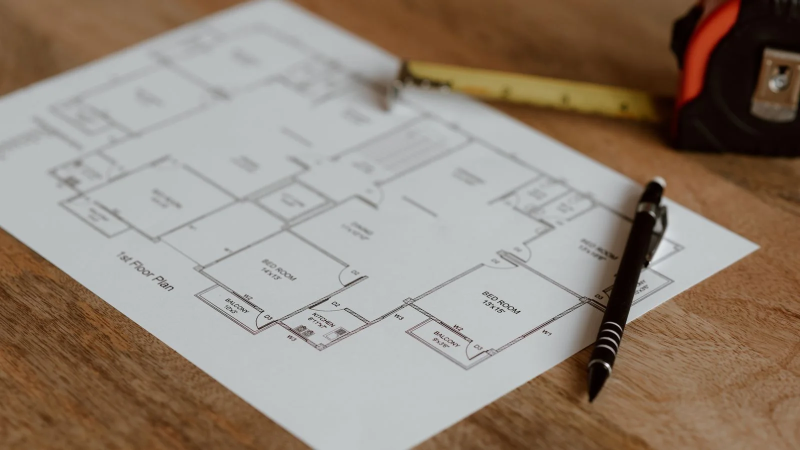 Plan architectural posé sur une table en bois avec un mètre ruban et un stylo.