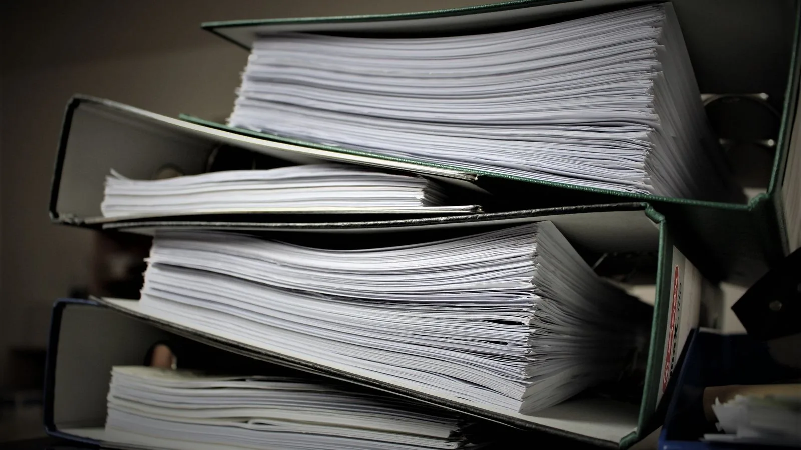 Une pile de classeurs remplis de documents administratifs sur une étagère.