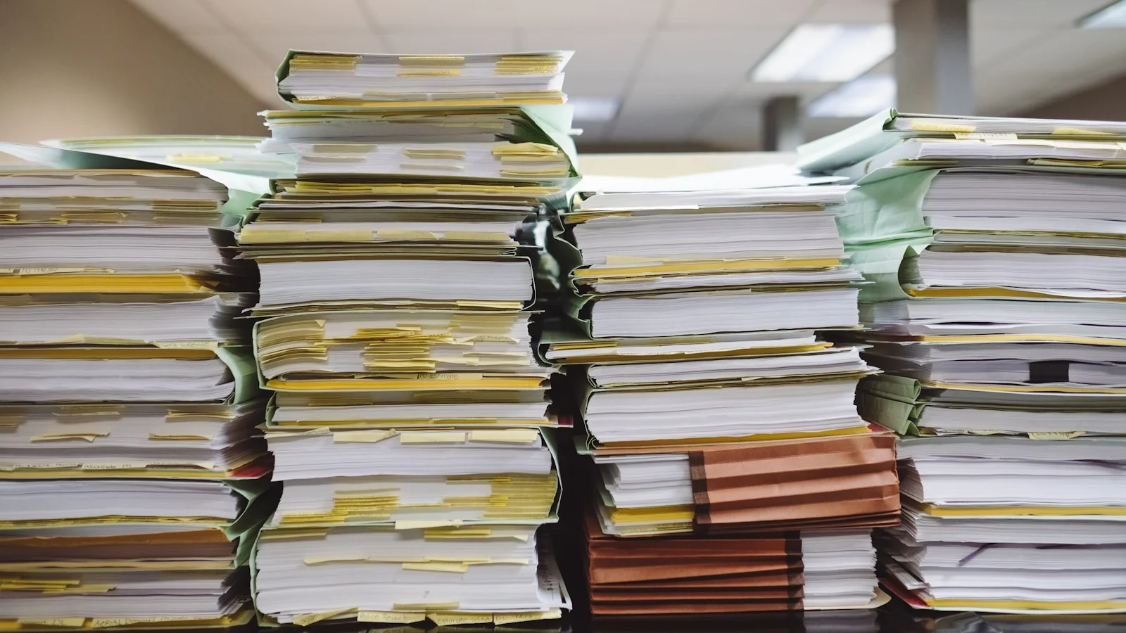 Pile de dossiers cartonnés et documents administratifs empilés sur un bureau, évoquant le travail concret de montage d'un dossier de chèque-entreprise.