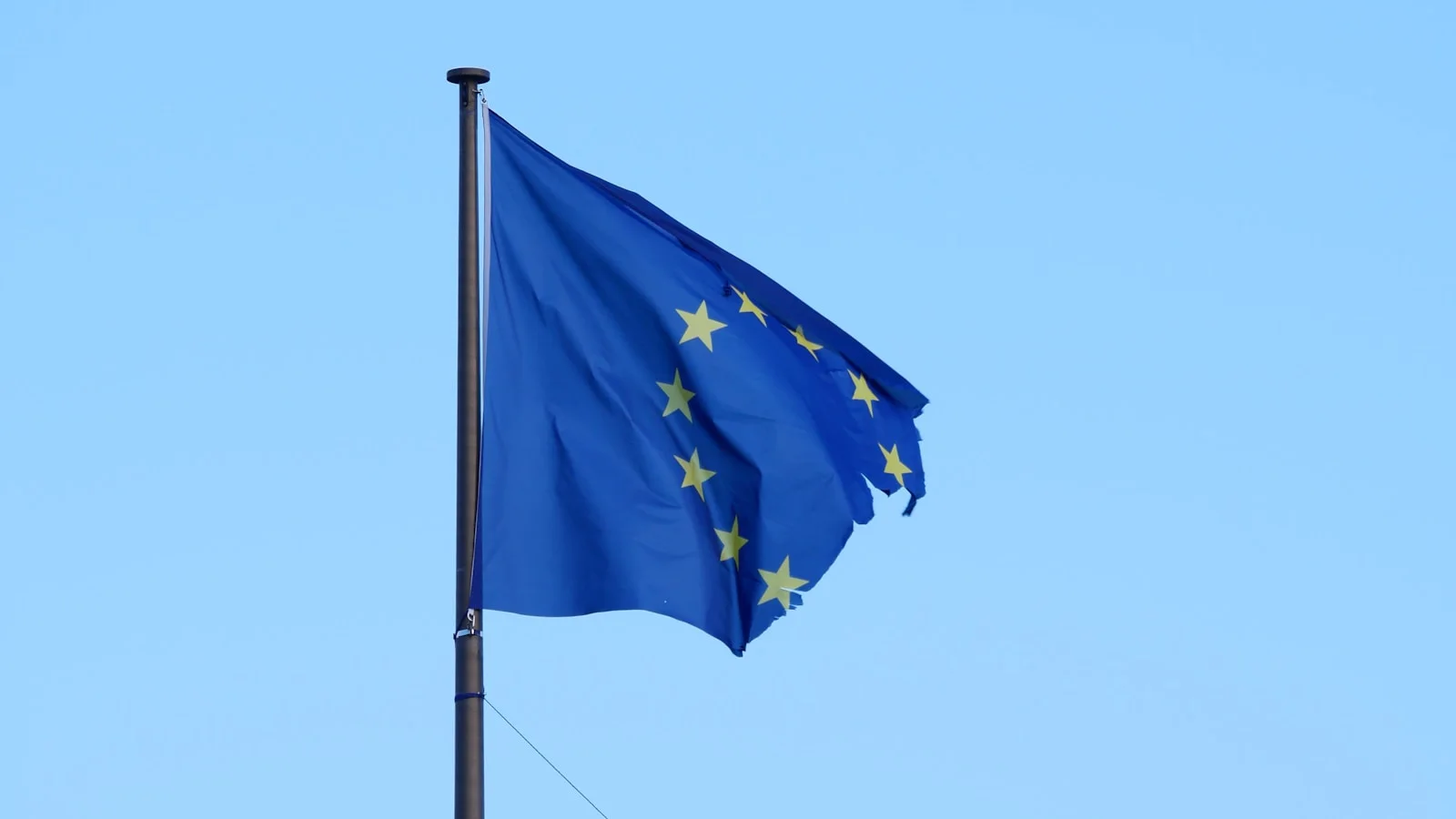 Drapeau de l'Union européenne flottant dans le vent sur fond de ciel clair, symbole des arbitrages politiques autour de la souveraineté numérique.