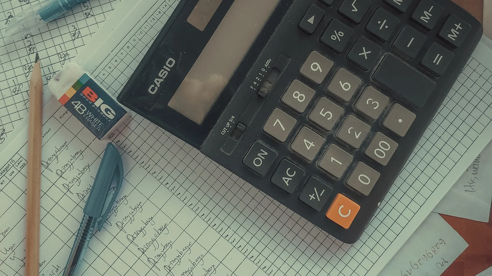 Calculatrice Casio posée sur un cahier de comptabilité manuscrit, avec stylo et gomme, évoquant le calcul réel d'un budget IA en PME.