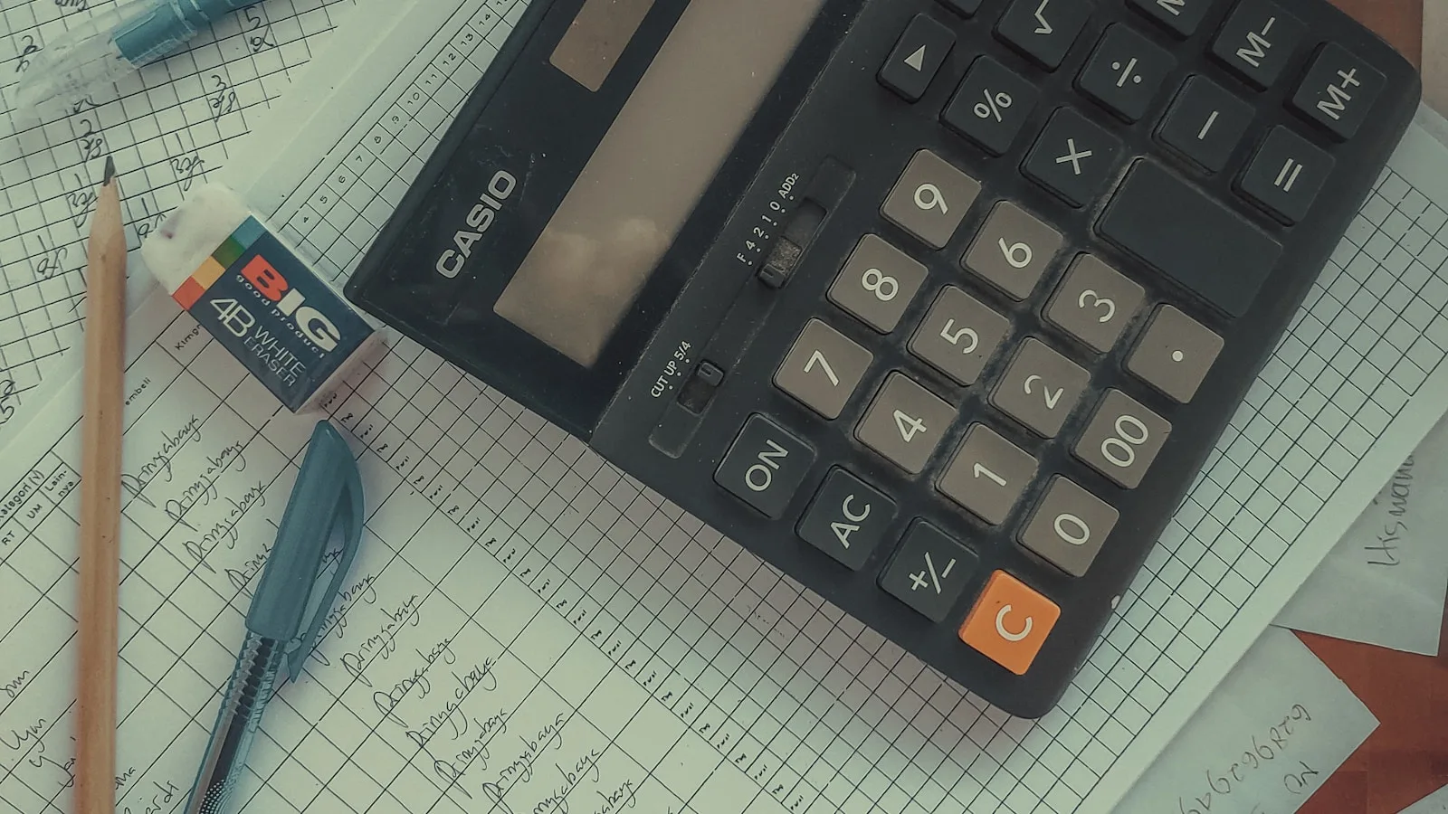 Calculatrice Casio posée sur un cahier de comptabilité manuscrit, avec stylo et gomme, évoquant le calcul réel d'un budget IA en PME.