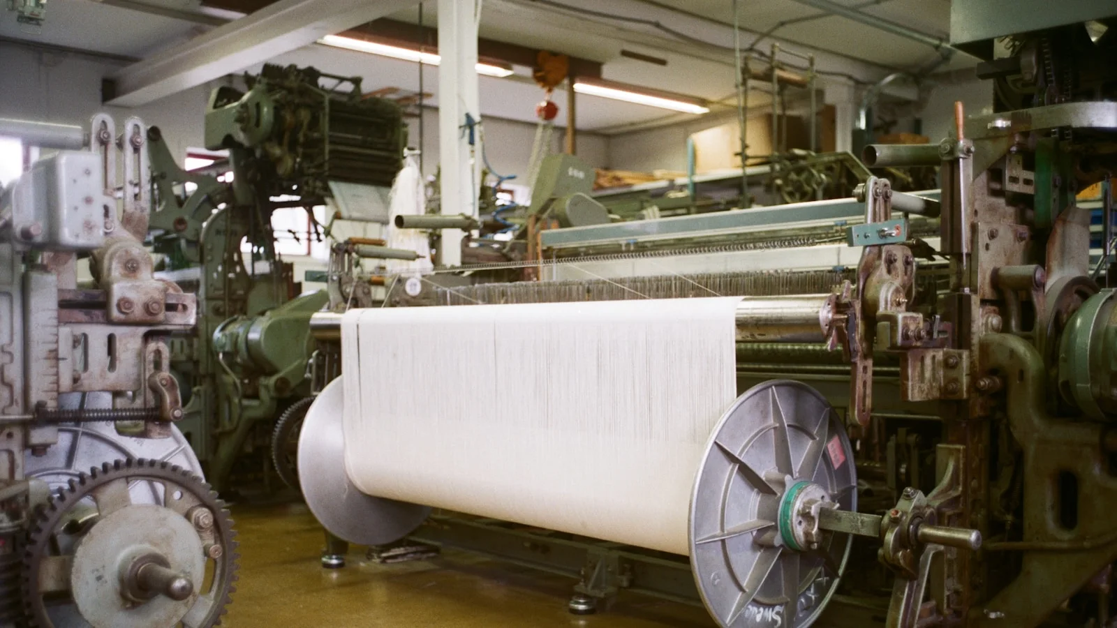 Métier à tisser industriel produisant une large bande de textile blanc.