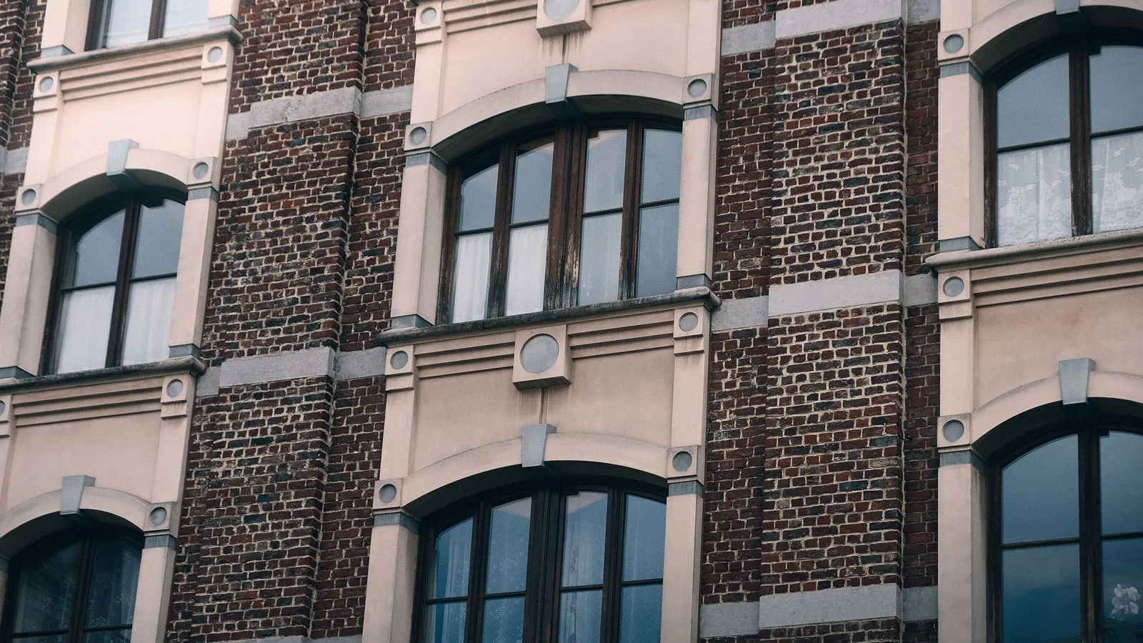 Façade en briques d’un immeuble résidentiel bruxellois aux fenêtres cintrées.
