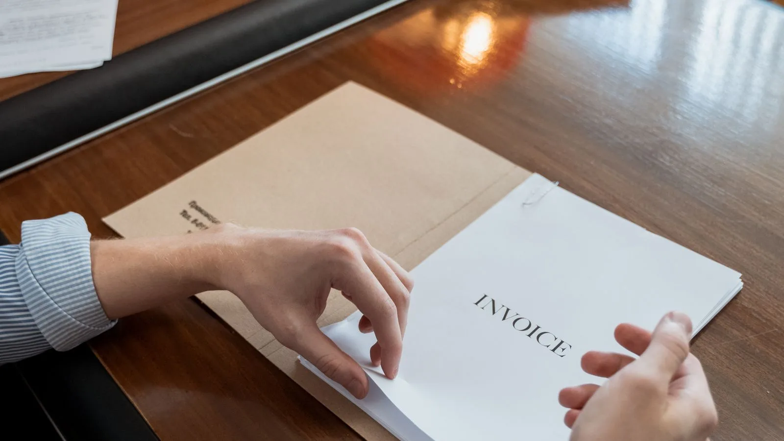 Des factures imprimées sont triées sur un bureau en bois.