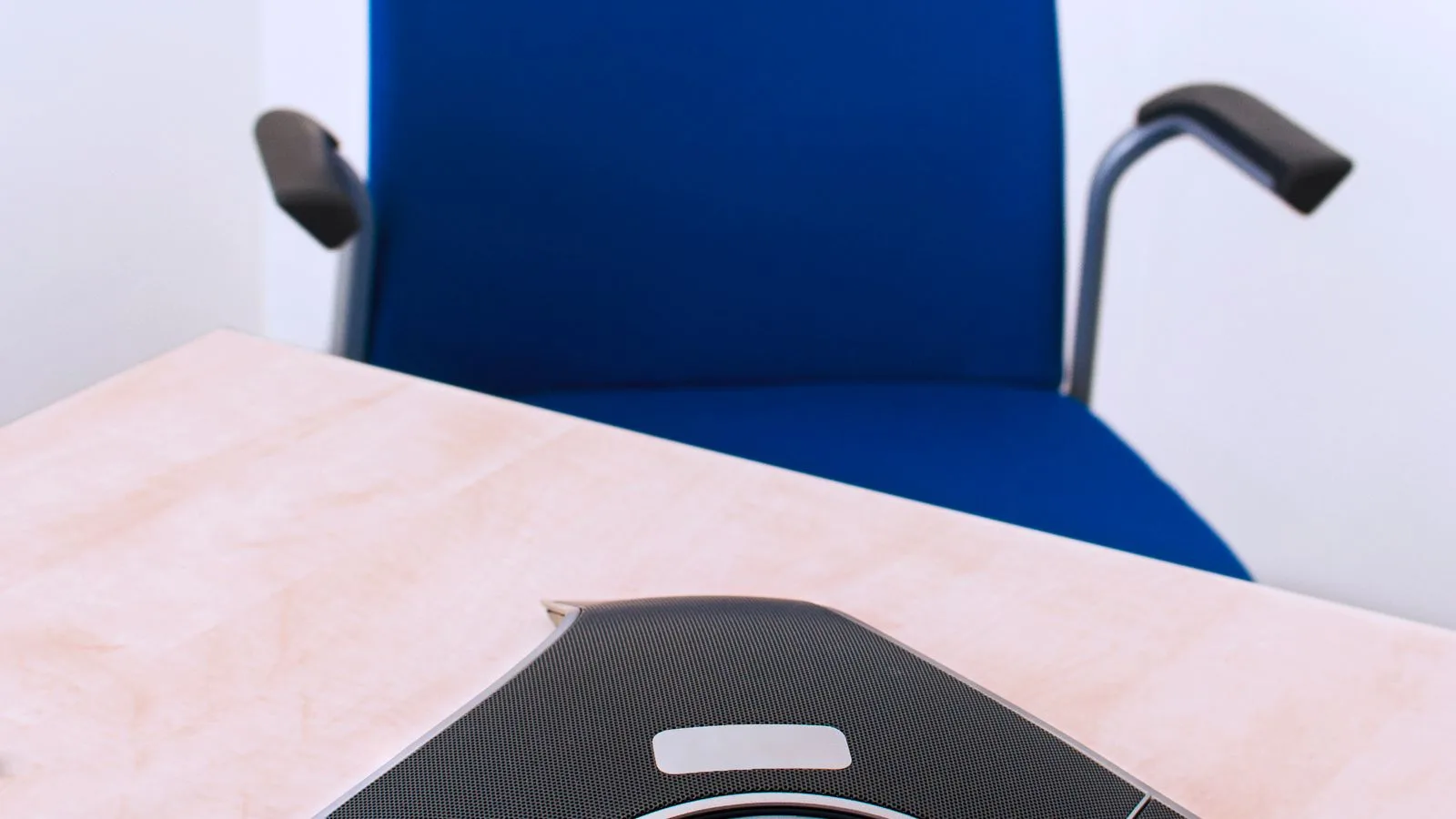 Téléphone de conférence posé sur une table devant une chaise vide.